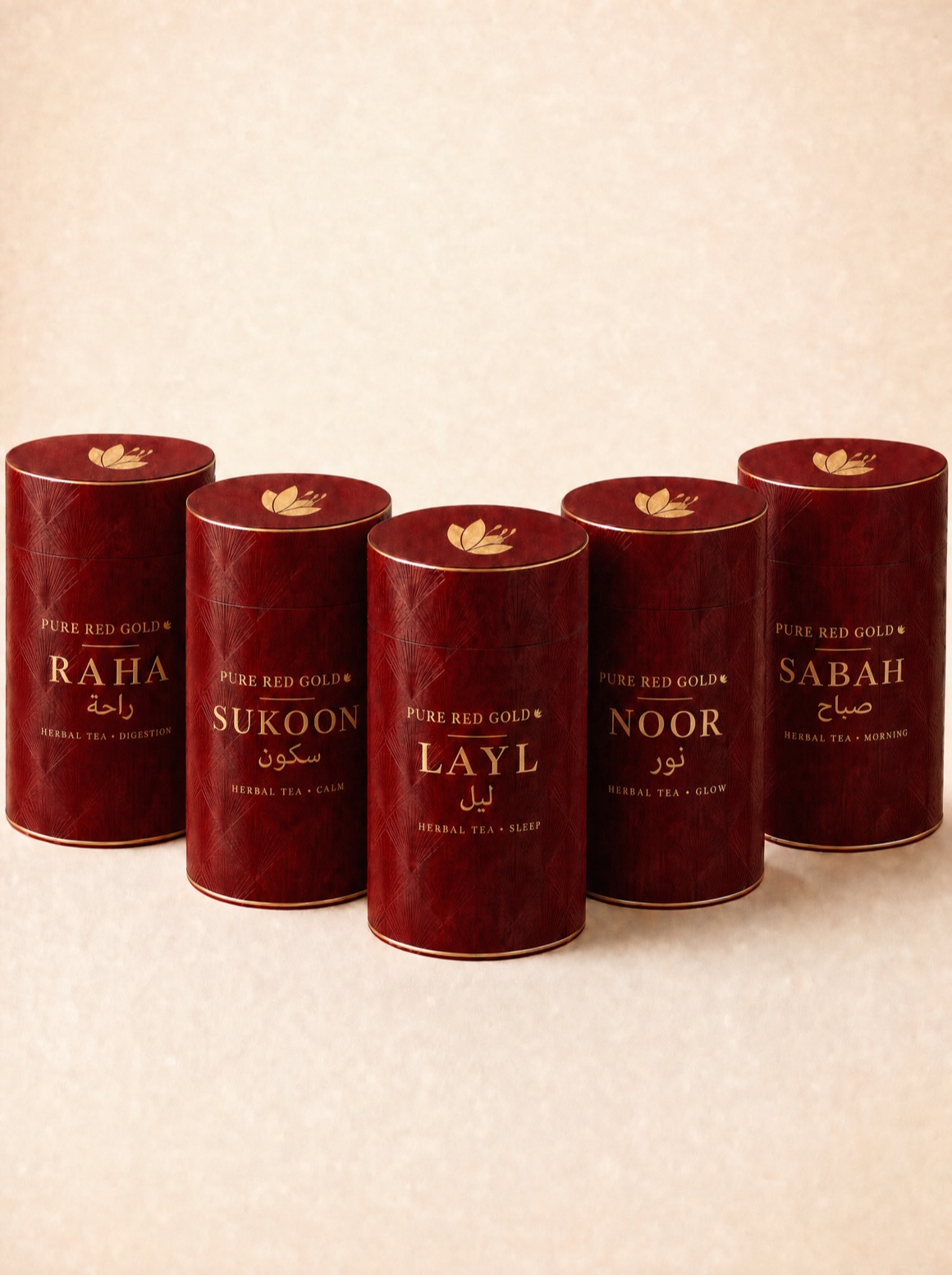 All five Pure Red Gold herbal tea tubes — crimson cylinders with an embossed art-deco pattern and a gold crocus on each lid, Layl in front with Sukoon, Noor, Raha and Sabah around it, on warm ivory